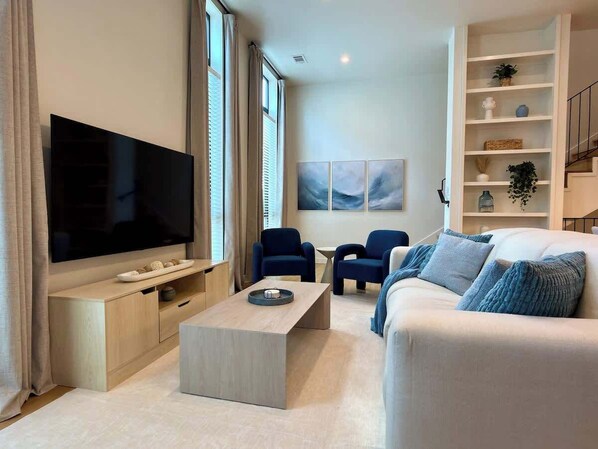 En moderne stue med et fladskærms-tv, et sofabord, en sofa og to lænestole.