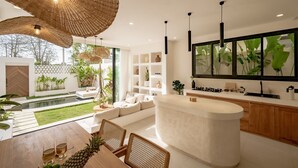 Una cocina moderna con una isla grande, un comedor con mesa y sillas, y vistas a un jardín.