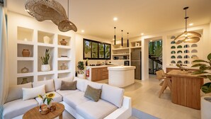 Una sala de estar moderna con un sofá, una mesa de centro y objetos decorativos. Hay una zona de cocina con una isla central, y un comedor con una mesa y sillas de madera.