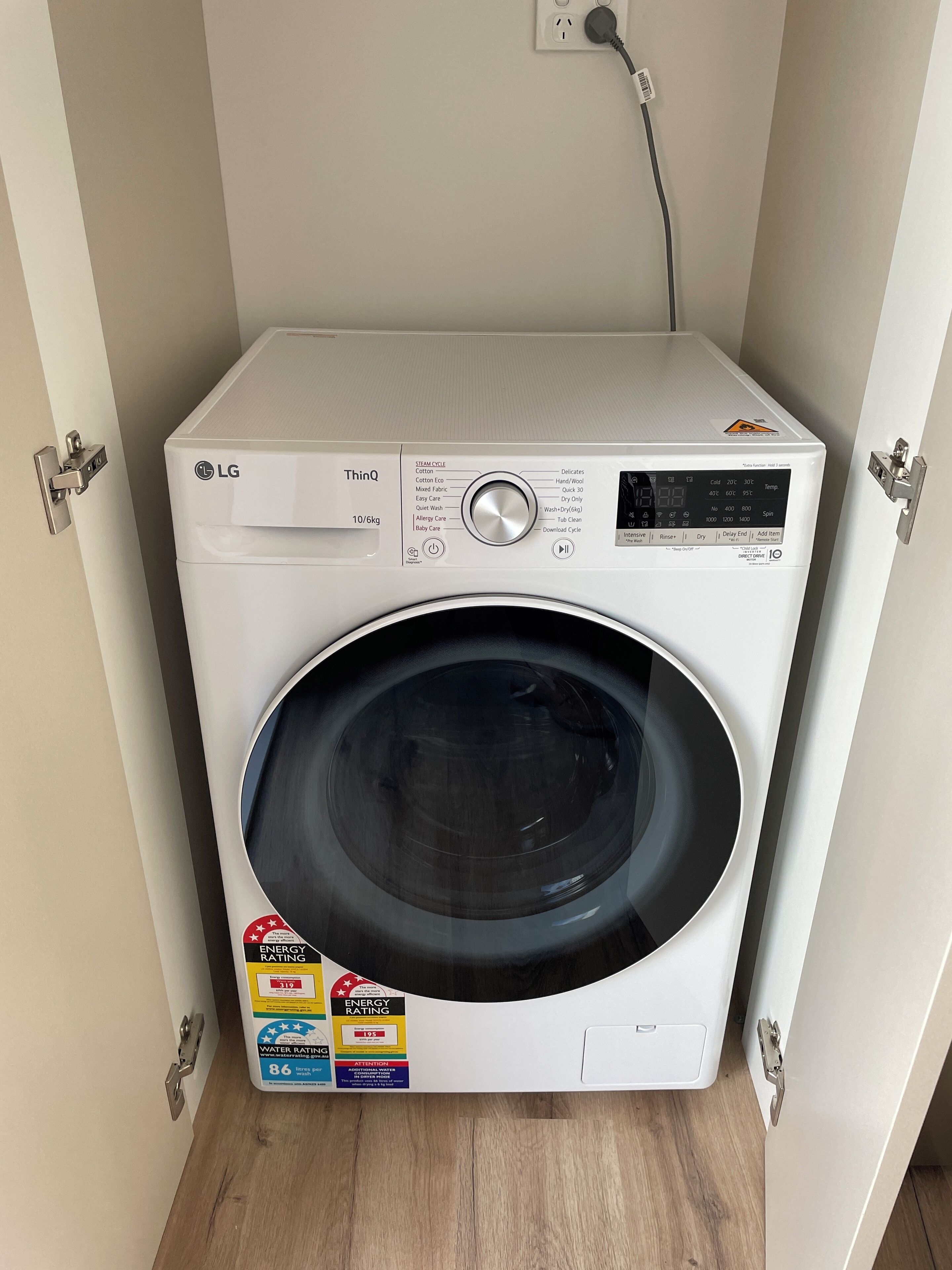 A front view of a white LG ThinQ washing machine with a control panel, energy and water rating labels, and a power cord plugged in.