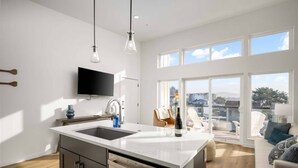 Una cocina moderna con una isla grande, un televisor de pantalla plana y vistas al exterior a través de amplios ventanales.
