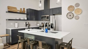 Una cocina moderna con armarios oscuros, una isla blanca, electrodomésticos de acero inoxidable y una zona de asientos con taburetes de bar.
