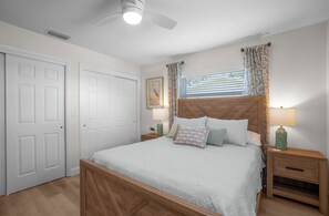A bedroom with a wooden bed, two nightstands, a ceiling fan, and a window with curtains.