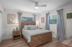 A bedroom with a wooden bed, two bedside tables, a ceiling fan, and framed artwork on the walls.