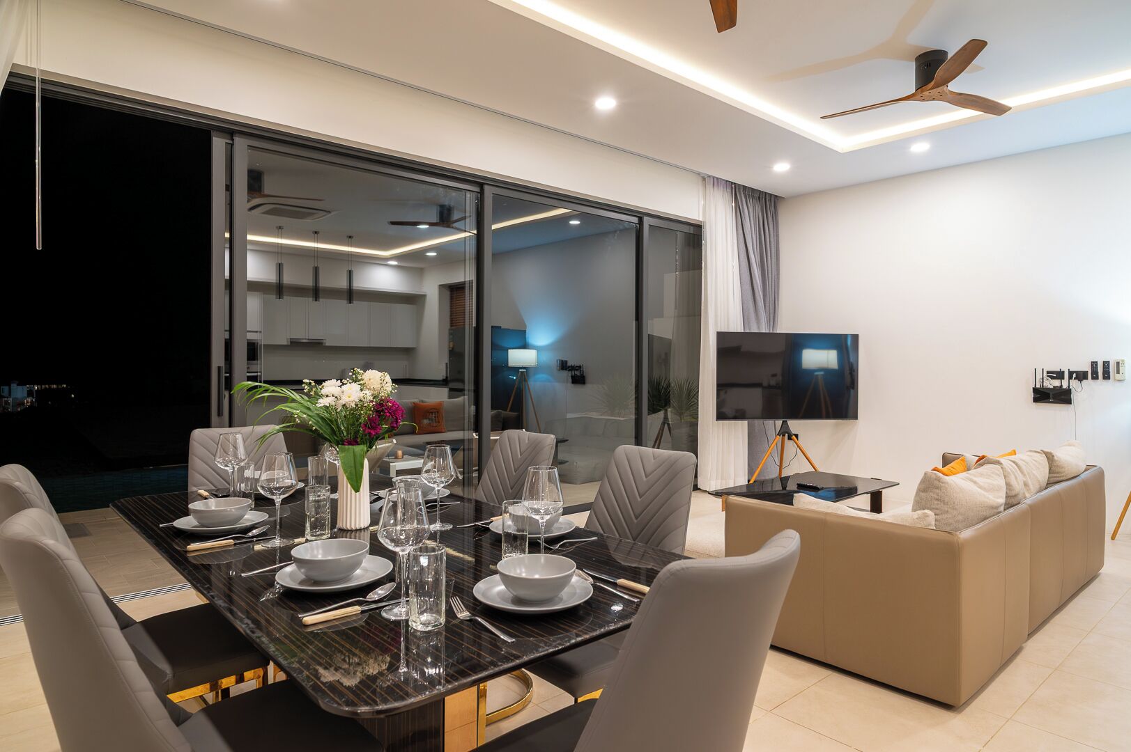 A modern dining area with a glass partition, a dining table set for six, and a sofa in the background.
