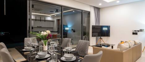 A modern dining area with a glass partition, a dining table set for six, and a sofa in the background.
