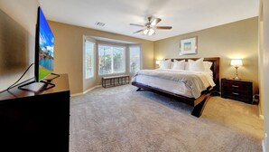 A bedroom with a bed, a ceiling fan, a nightstand with a lamp, a bench, and a TV on a stand.