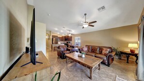 A spacious living room with a large wooden coffee table, leather sofas, and a flat-screen TV.