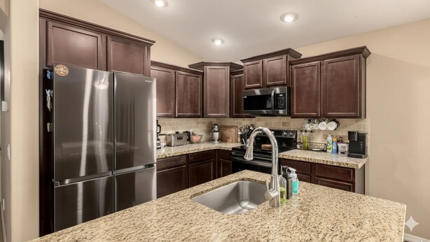 A kitchen with dark wood cabinets, stainless steel appliances, granite countertops, and a sink with a faucet.