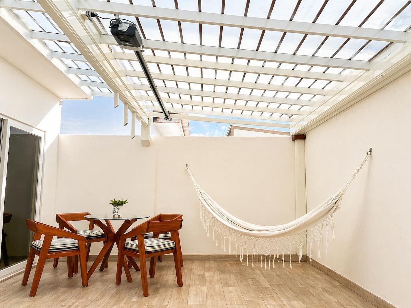 Une terrasse avec une table et des chaises, un hamac et une pergola dotée d’un ventilateur de plafond.
