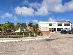 Um edifício com fachada branca, um mastro de bandeira e um estacionamento com carros.