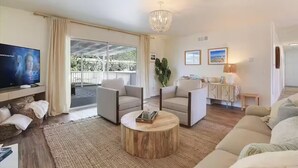 A spacious living room with a large TV, two sofas, a coffee table, and a balcony with a view of greenery. - Spa, Beaches, Wine Country: Santa Barbara Coastal Escape for Friends and Family (Goleta)