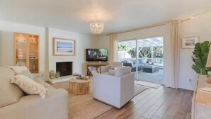 A modern living room with a fireplace, a television, and a view of the outdoor patio. - Spa, Beaches, Wine Country: Santa Barbara Coastal Escape for Friends and Family (Goleta)
