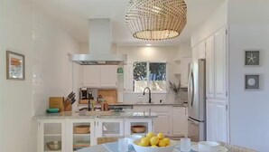 A modern kitchen with white cabinetry, a central island with a bowl of lemons, and a hanging light fixture. - Spa, Beaches, Wine Country: Santa Barbara Coastal Escape for Friends and Family (Goleta)