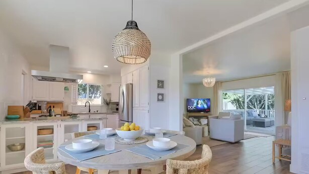 A modern kitchen with white cabinets, a dining area with a round table, wicker chairs, and a hanging light fixture. - Spa, Beaches, Wine Country: Santa Barbara Coastal Escape for Friends and Family (Goleta)
