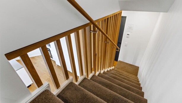Un escalier avec des rampes en bois et des marches recouvertes de moquette, menant à une pièce dont la porte est blanche.