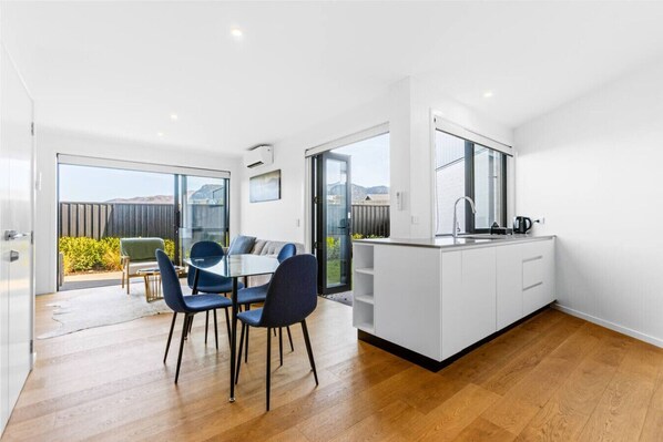 A modern kitchen with a large island, a dining area with blue chairs, and a sliding glass door leading to a balcony. - Modern Townhouse, Alpine Views, Close To Wanaka (Wānaka)