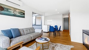 Uma sala de estar moderna com um sofá cinzento, cadeiras azuis, uma mesa de centro e uma lareira.