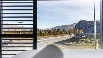 Vista des de dins d'una habitació, amb una finestra que dona a un carrer i muntanyes.