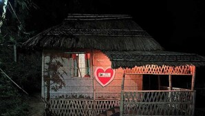 Une petite cabane à toit de chaume, ornée d’une enseigne en forme de cœur sur le mur, avec une véranda en bois et un escalier menant à l’entrée.