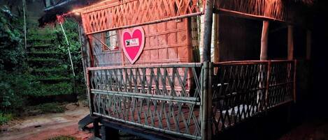 A small, rustic wooden structure with a heart-shaped sign on the side, surrounded by greenery.