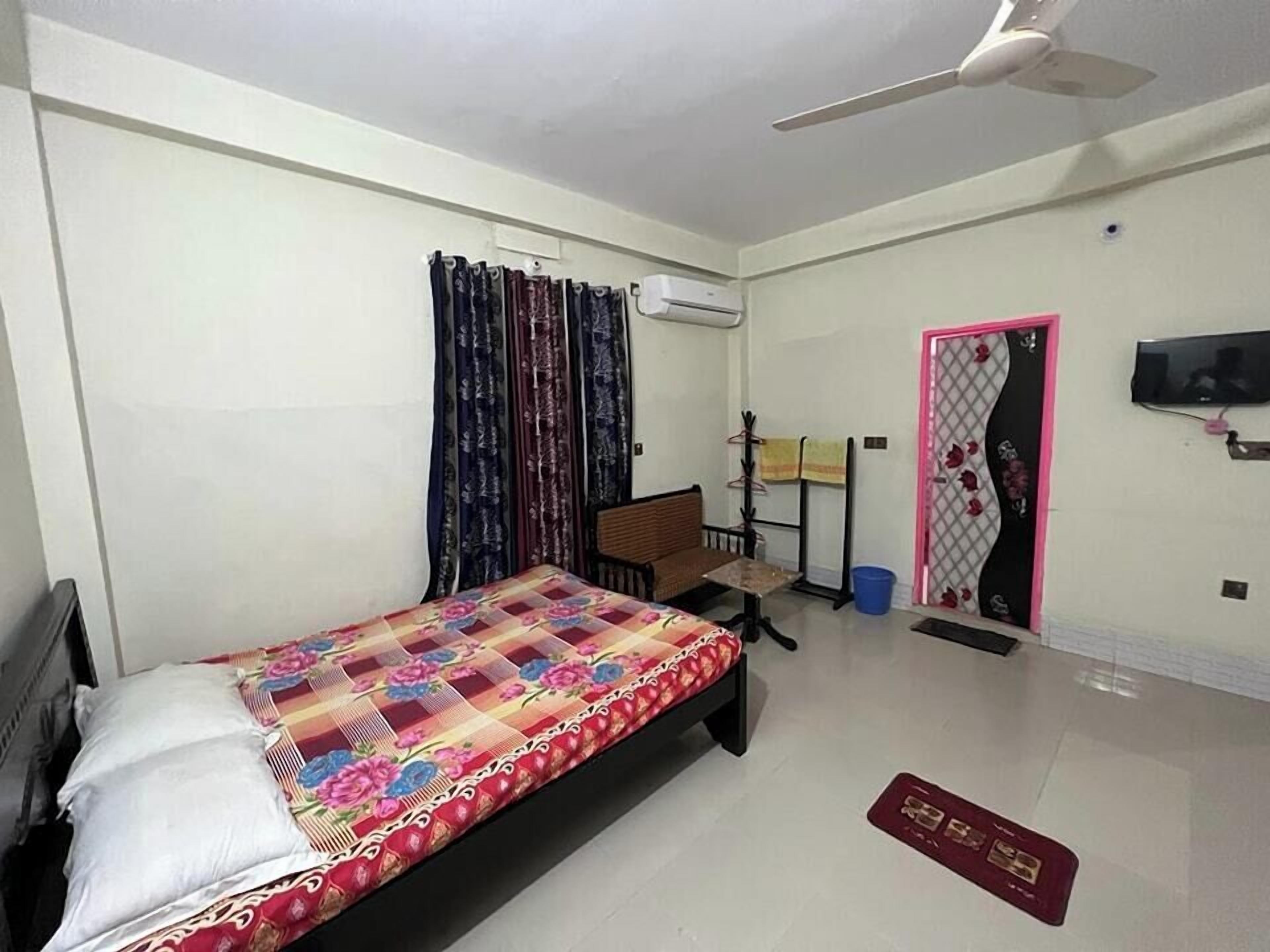 Un dormitorio con una cama, un escritorio, una silla, aire acondicionado, un televisor y una puerta con un diseño decorativo.