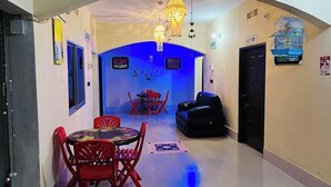 Un couloir étroit mène à un espace repas agrémenté d’une table ronde et de chaises rouges, d’un canapé noir et d’un mur éclairé en bleu.