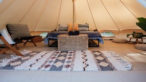 A cozy tent interior with a bed, pillows, a woven stool, and a patterned rug. - Romantic Queen Bed Glamping Tent (Tomerong)
