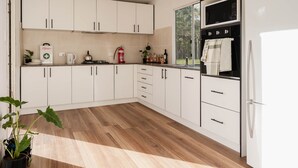 A modern kitchen with white cabinets, a microwave, oven, and a refrigerator. There is a wooden floor and a potted plant. - Romantic Queen Bed Glamping Tent (Tomerong)