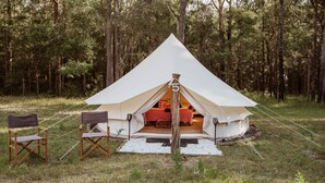 Une tente en forme de dôme avec un lit à l’intérieur, entourée d’une forêt. Deux chaises pliantes se trouvent à l’extérieur de la tente.
