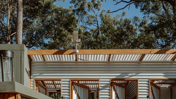 Une cabane moderne et compacte, dotée d’une terrasse en bois, de murs en métal et de grandes fenêtres.