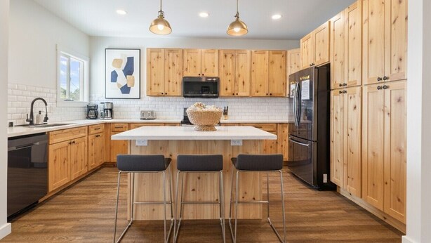 A modern kitchen with wooden cabinets, a central island with stools, stainless steel appliances, and pendant lighting.