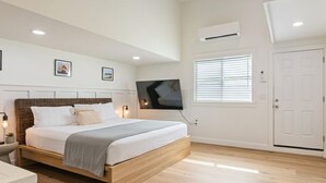 A bedroom with a wooden bed, white walls, a mounted TV, and a door.