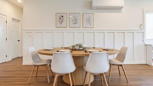 A dining area with a round wooden table, white chairs, and three framed botanical prints on the wall.