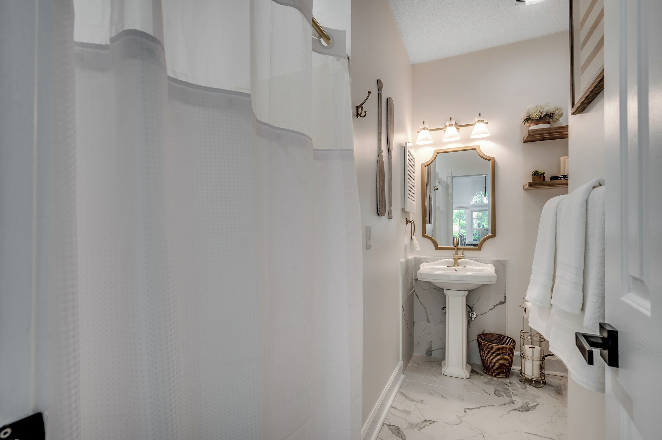 A bathroom with a white sink, a mirror with lights, a shower curtain, and a towel rack.