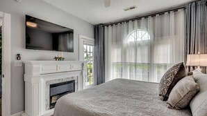 Un dormitorio con una cama grande, chimenea, televisión y vistas al exterior.