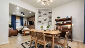 A modern living room with a wooden dining table, chairs, and a patterned rug. There is a TV mounted on the wall and a bookshelf with decorative items. - HostWise Stays - Firepit | Sauna | Driveway | Hammock | King Beds (Pittsburgh)
