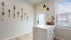 A modern kitchen with a marble countertop, wooden utensils hanging on the wall, and a window with blinds. - HostWise Stays - Firepit | Sauna | Driveway | Hammock | King Beds (Pittsburgh)