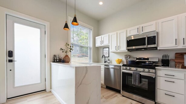 A modern kitchen with white cabinets, stainless steel appliances, and a marble island. - HostWise Stays - Firepit | Sauna | Driveway | Hammock | King Beds (Pittsburgh)
