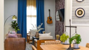 A cozy living room with a wooden coffee table, a brown leather sofa, and a blue curtain. - HostWise Stays - Firepit | Sauna | Driveway | Hammock | King Beds (Pittsburgh)