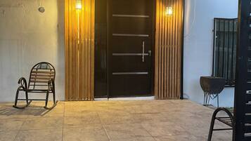 Puerta de madera con un panel negro y una manija, flanqueada por listones de madera verticales y dos luces fijadas a la pared.