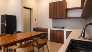 Una cucina compatta con un tavolo da pranzo in legno, sedie, un piano cottura integrato e un frigorifero nero.