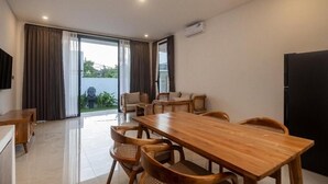 Un'area pranzo moderna con tavolo e sedie in legno, televisione e una porta vetrata scorrevole che dà su un balcone.
