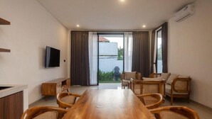 Una camera moderna con un tavolo da pranzo in legno, sedie in vimini, un divano e una TV a parete.