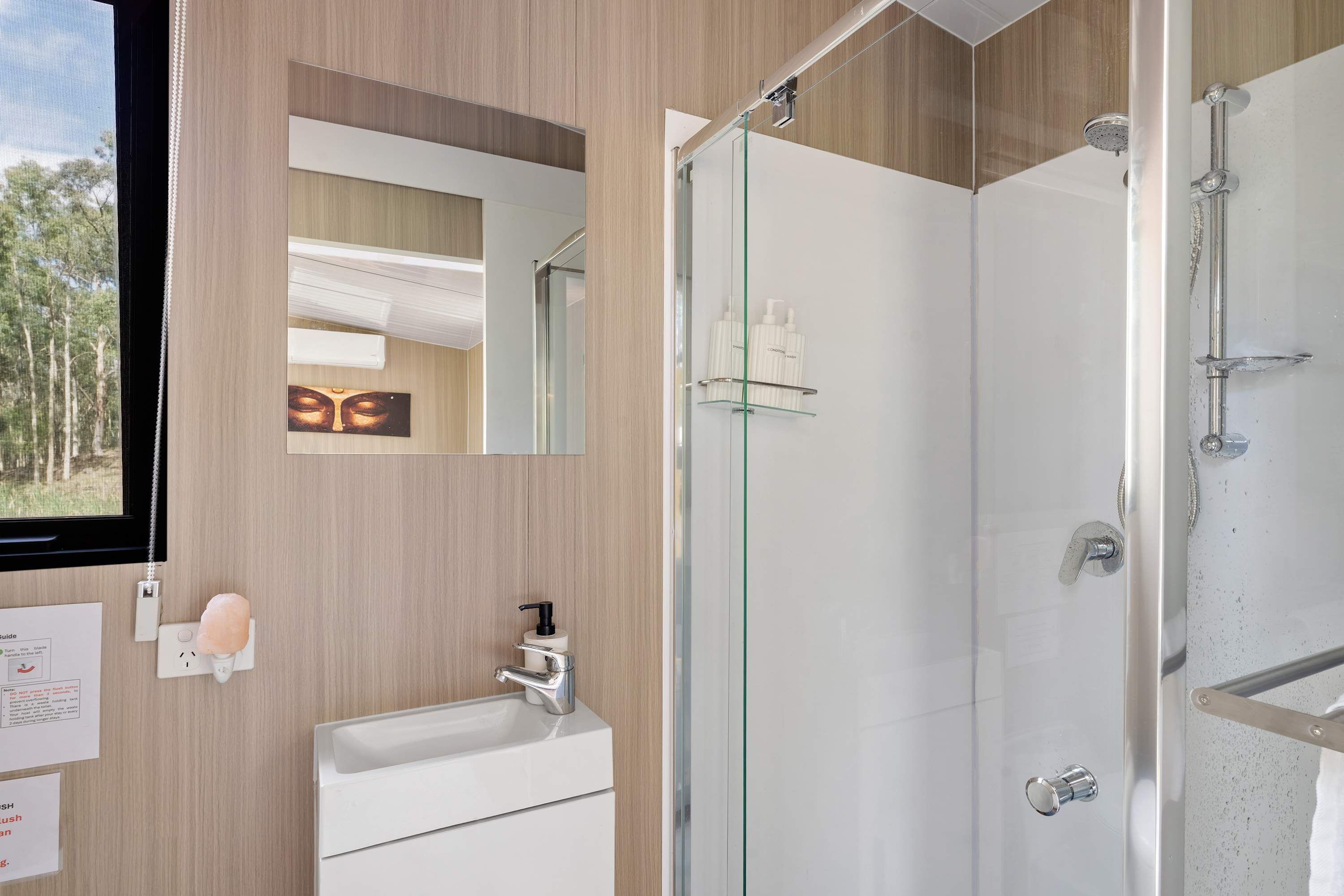 A modern bathroom with a glass shower enclosure, a white sink, and a mirror.