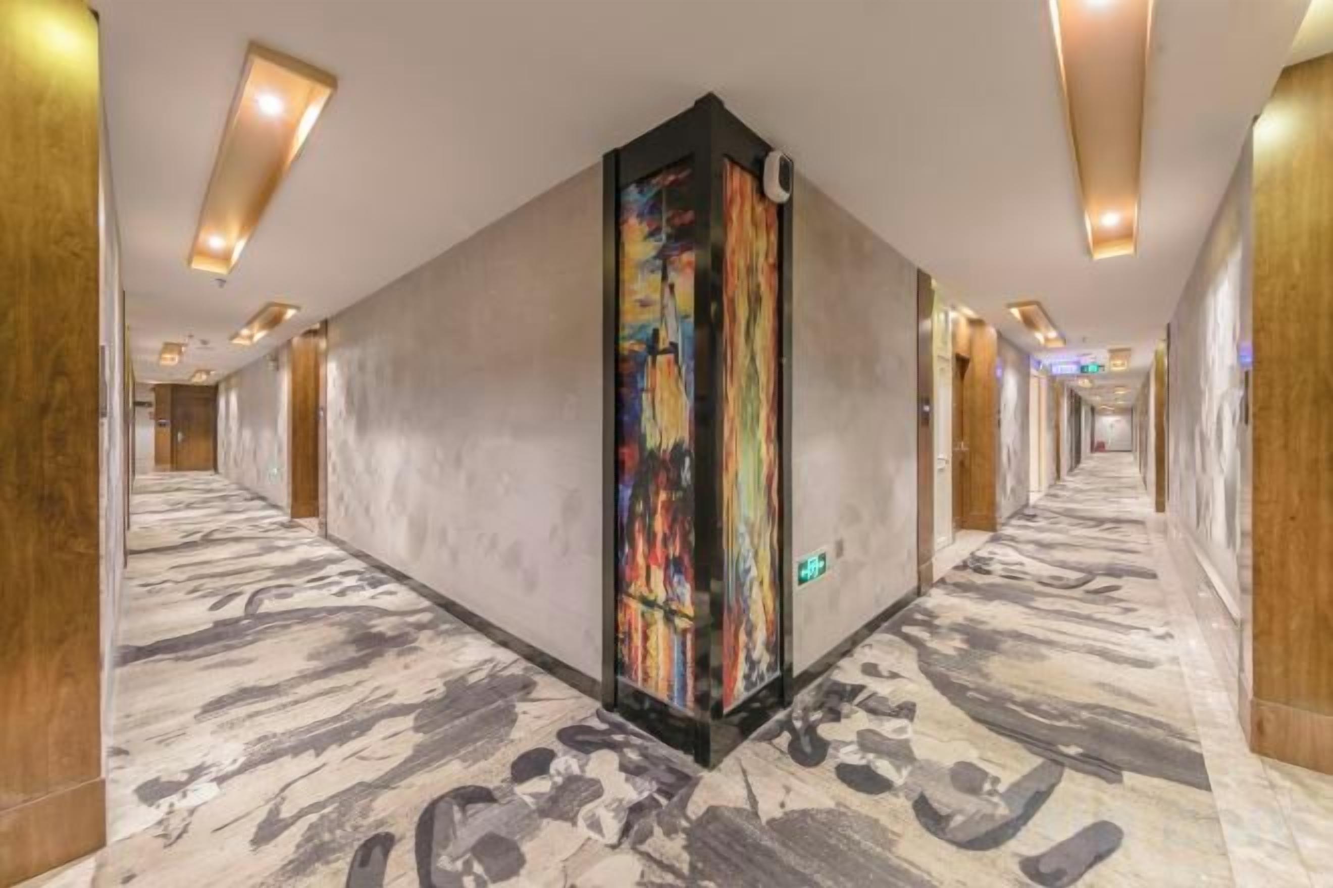Un pasillo de hotel con piso de mármol, paredes de madera y una obra de arte vertical colorida.