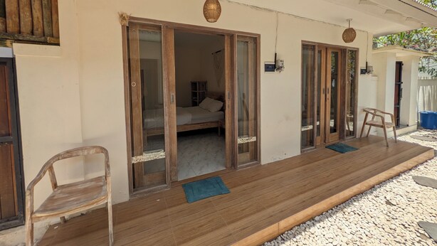 A wooden-framed room with a bed, a chair, and a small table. - Luma Guesthouse by Verdana Homes (Tibubeneng)