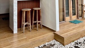 A modern kitchen with wooden cabinets, a marble countertop, and two stools. - Luma Guesthouse by Verdana Homes (Tibubeneng)