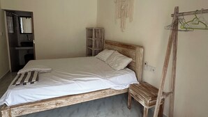 A bedroom with a wooden bed, a small wooden stool, a wardrobe, and a macrame wall hanging. - Luma Guesthouse by Verdana Homes (Tibubeneng)