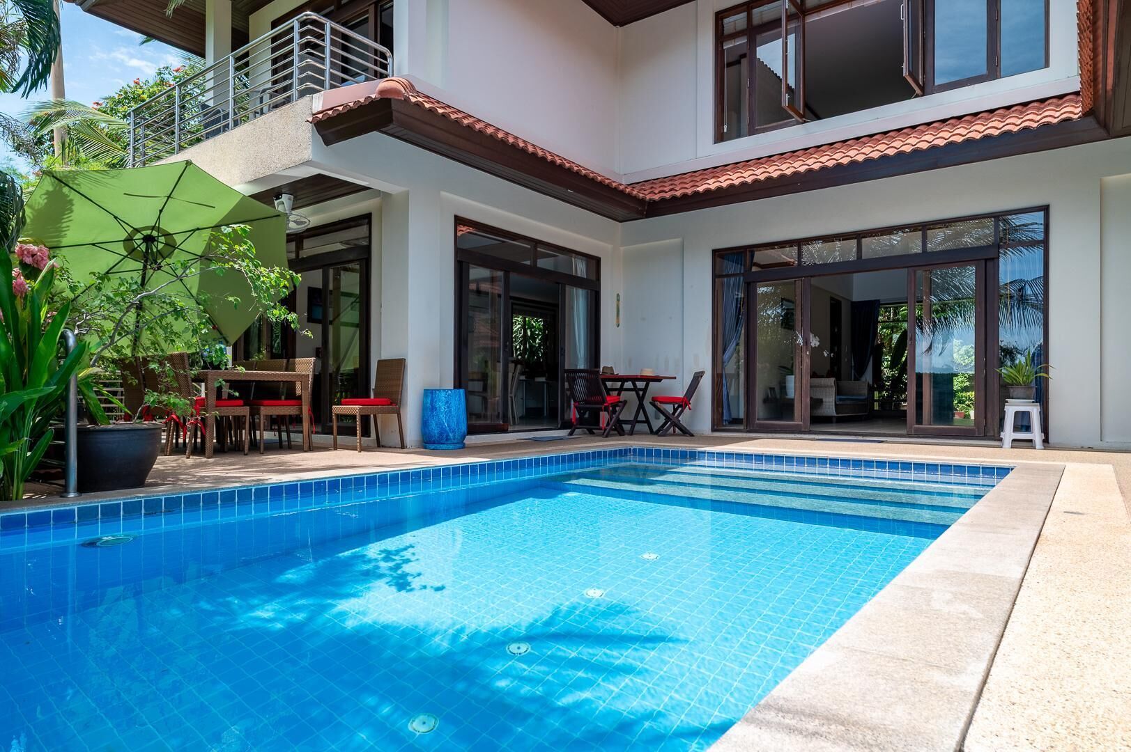 Una casa moderna con piscina, mobiliario exterior y balcón.